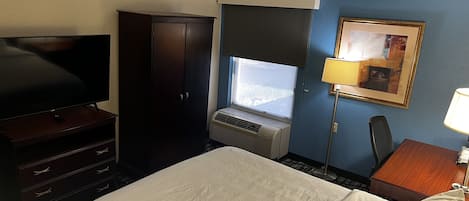 A hotel room with a bed, a TV, a wardrobe, a desk with a lamp, and a window with a view.