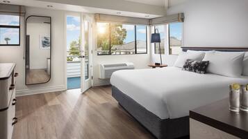 Une chambre moderne dotée d’un grand lit, d’un dressing, d’une salle de bain et d’un balcon offrant une vue sur le quartier.
