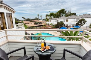 Un balcón con una mesa preparada para el desayuno, con vista a una piscina y edificios residenciales.