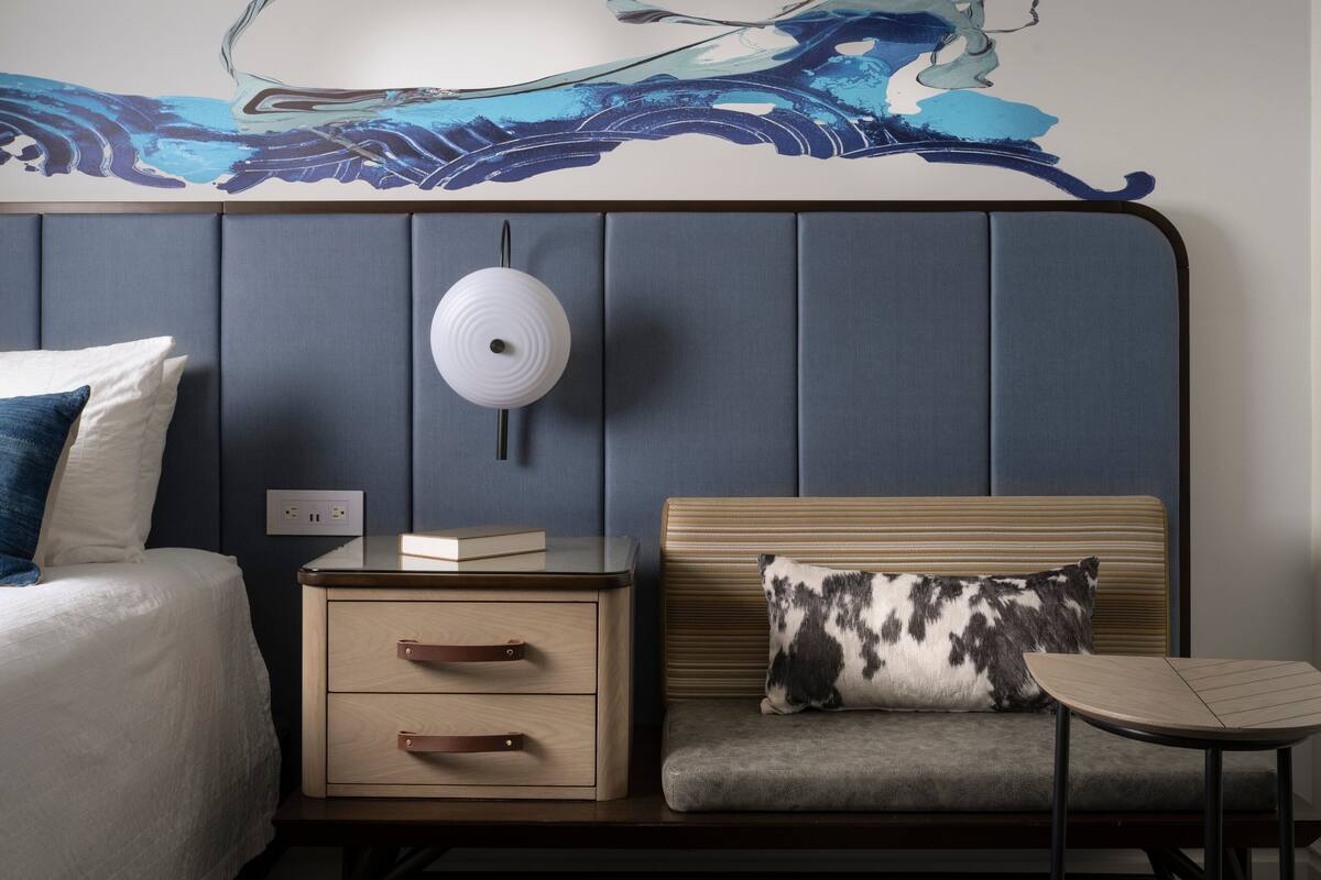 Een hotelkamer met een bed, nachtkastje, en een zithoek met een kussen.