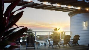 Une terrasse avec des chaises et une table, d’où l’on peut admirer un coucher de soleil sur une étendue d’eau.