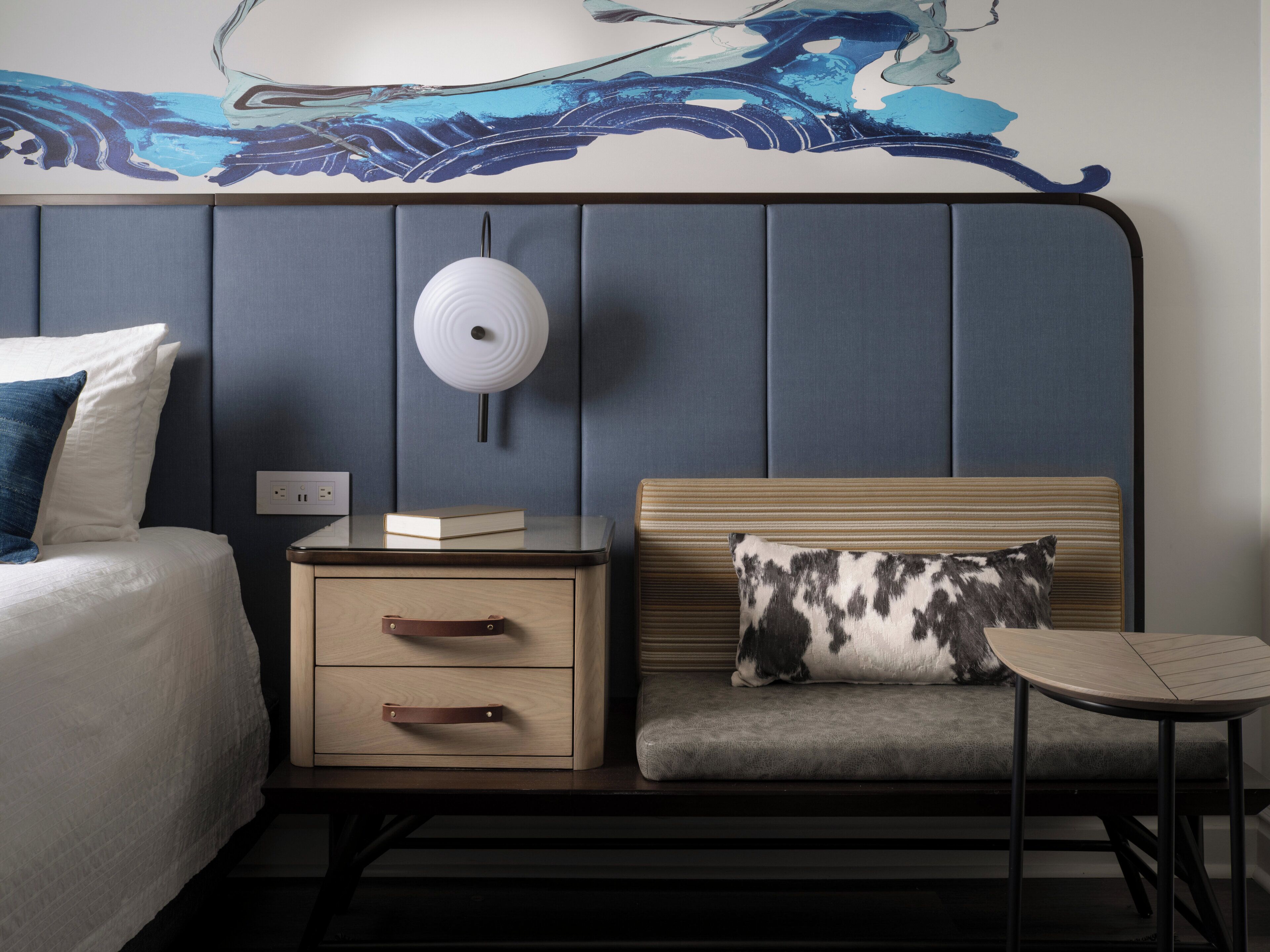 Une chambre d’hôtel comprenant un lit, une table de chevet, une lampe, une commode et une petite table avec une chaise.