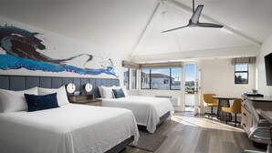 Une chambre d’hôtel moderne équipée de deux lits, d’un ventilateur de plafond, d’un bureau avec une chaise et d’une grande fenêtre donnant sur l’extérieur.