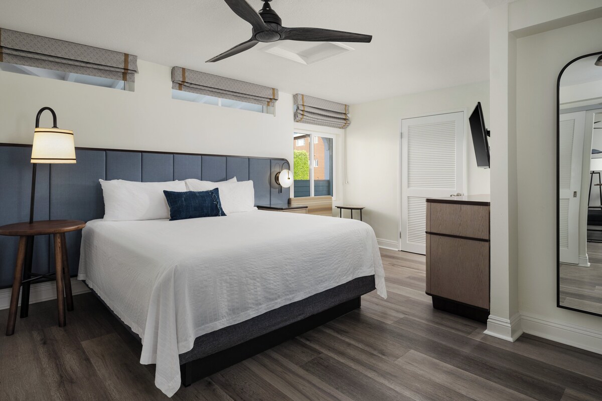 Ein Schlafzimmer mit einem Bett, Nachttischen, einem Deckenventilator, einem Schreibtisch und einem Spiegel.