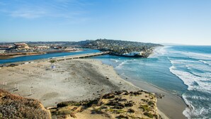 Une plage côtière offrant une vue dégagée sur l’océan, un pont et une ville située au loin.