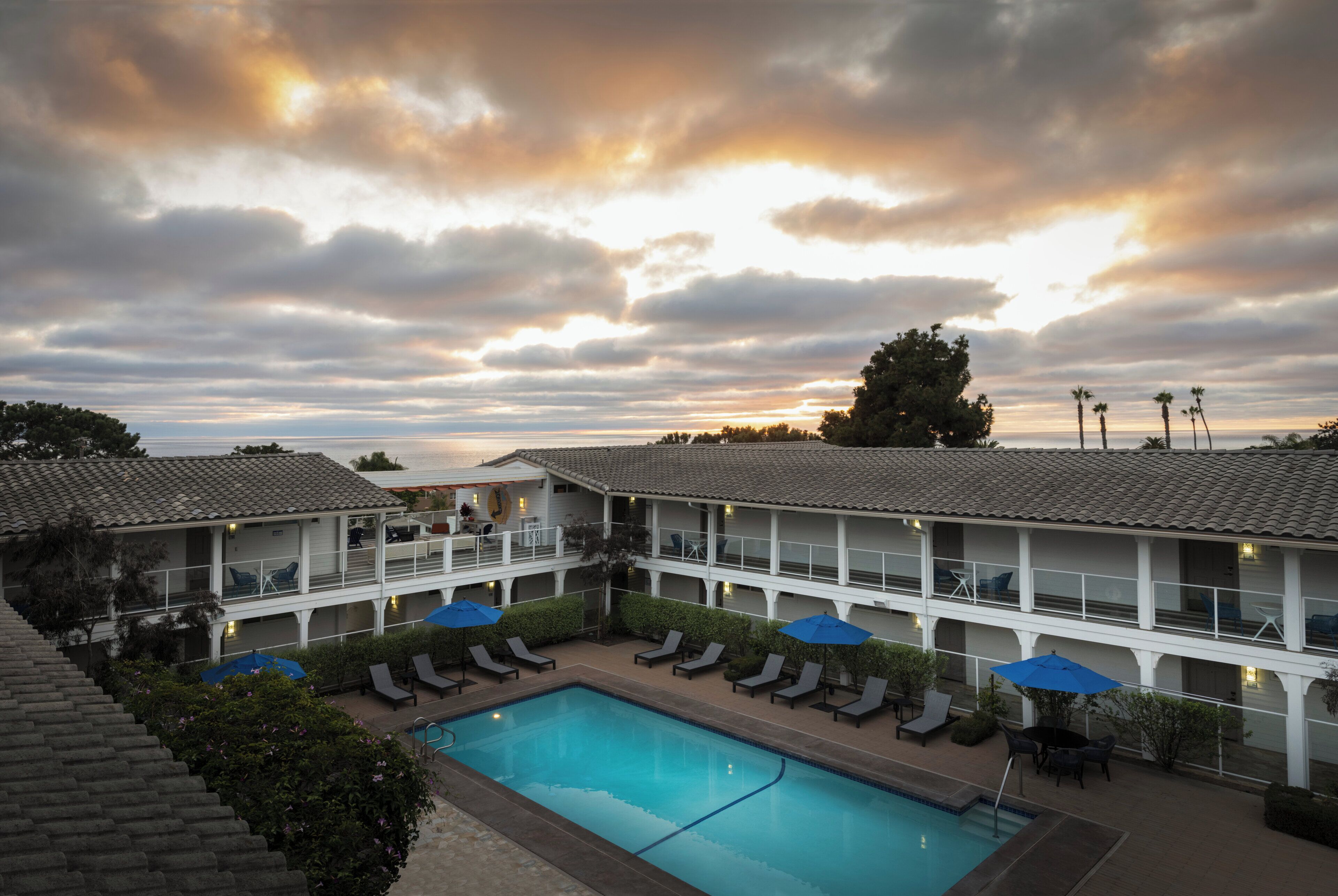 A hotel with a swimming pool, lounge chairs, and a sunset view.