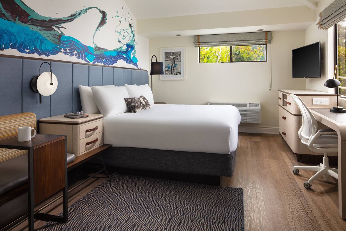 Een hotelkamer met een bed, bureau, stoel en een groot raam met uitzicht.