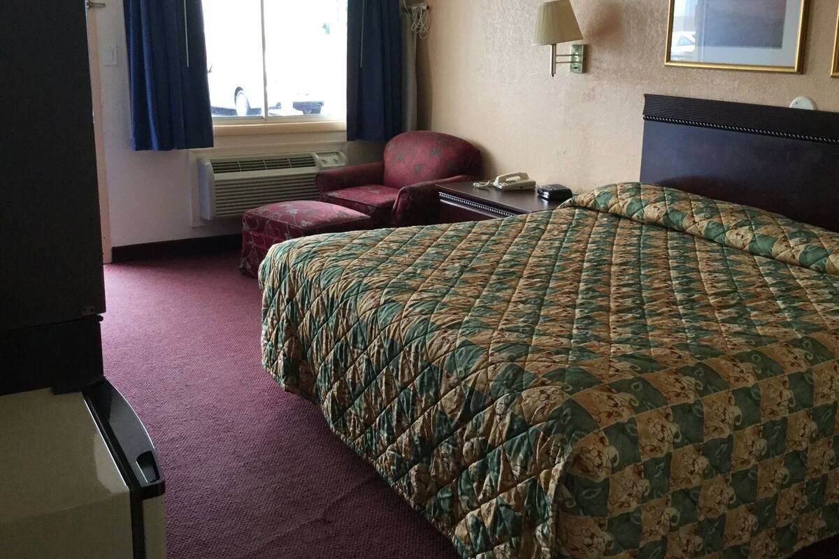 A hotel room with a bed, a chair, a desk, a telephone, and a window with curtains.