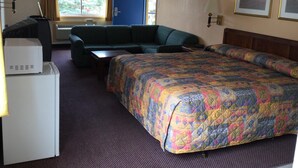 Ein Hotelzimmer mit einem Bett, einer Couch, einem Schreibtisch mit Computer und einem Fenster mit Vorhängen.