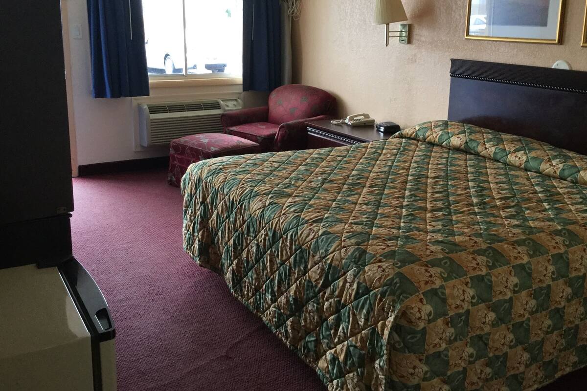 A hotel room with a bed, a chair, a desk, and a telephone.