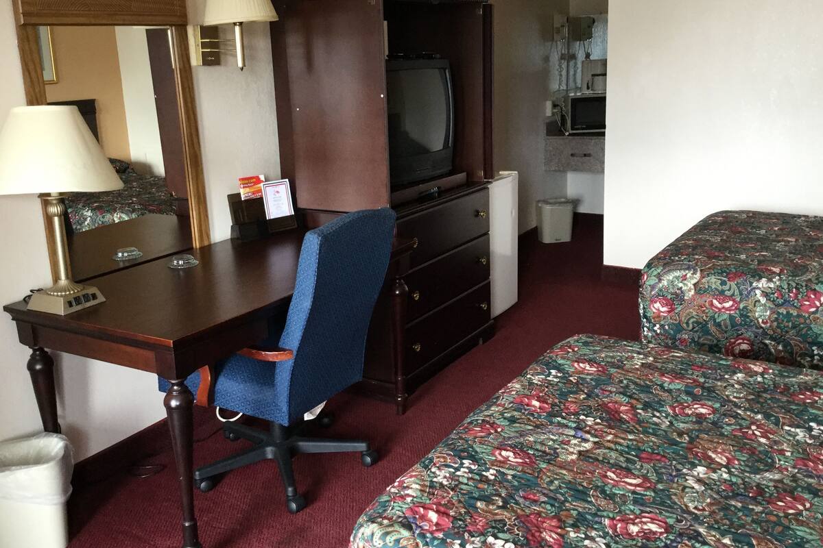 A hotel room with a desk, chair, television, and a bed with floral bedding.