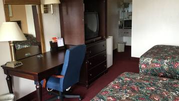 A hotel room with a desk, chair, television, and a bed with floral bedding.
