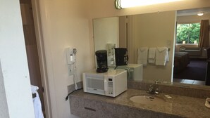 Ein Hotelbadezimmer mit einer Granit-Arbeitsplatte, einem weißen Waschbecken, einem Spiegel, einer Kaffeemaschine und einem Telefon.