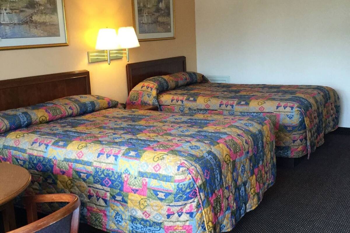 A hotel room with two beds, a chair, and two wall-mounted lamps.
