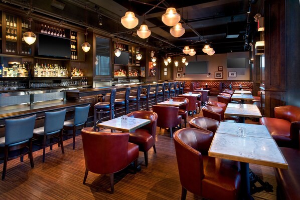 A restaurant with multiple tables and booths, wooden floors, and hanging pendant lights. - New York Marriott Downtown (New York)