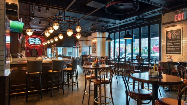 A restaurant interior with bar seating, tables, and hanging light fixtures. - New York Marriott Downtown (New York)