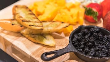 A wooden cutting board with grilled potato wedges, mango chunks, and a bowl of blackberries.