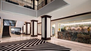 A spacious lobby with a large black and white patterned carpet, a reception desk with a marble counter, and a staircase leading to an upper level. - New York Marriott Downtown (New York)