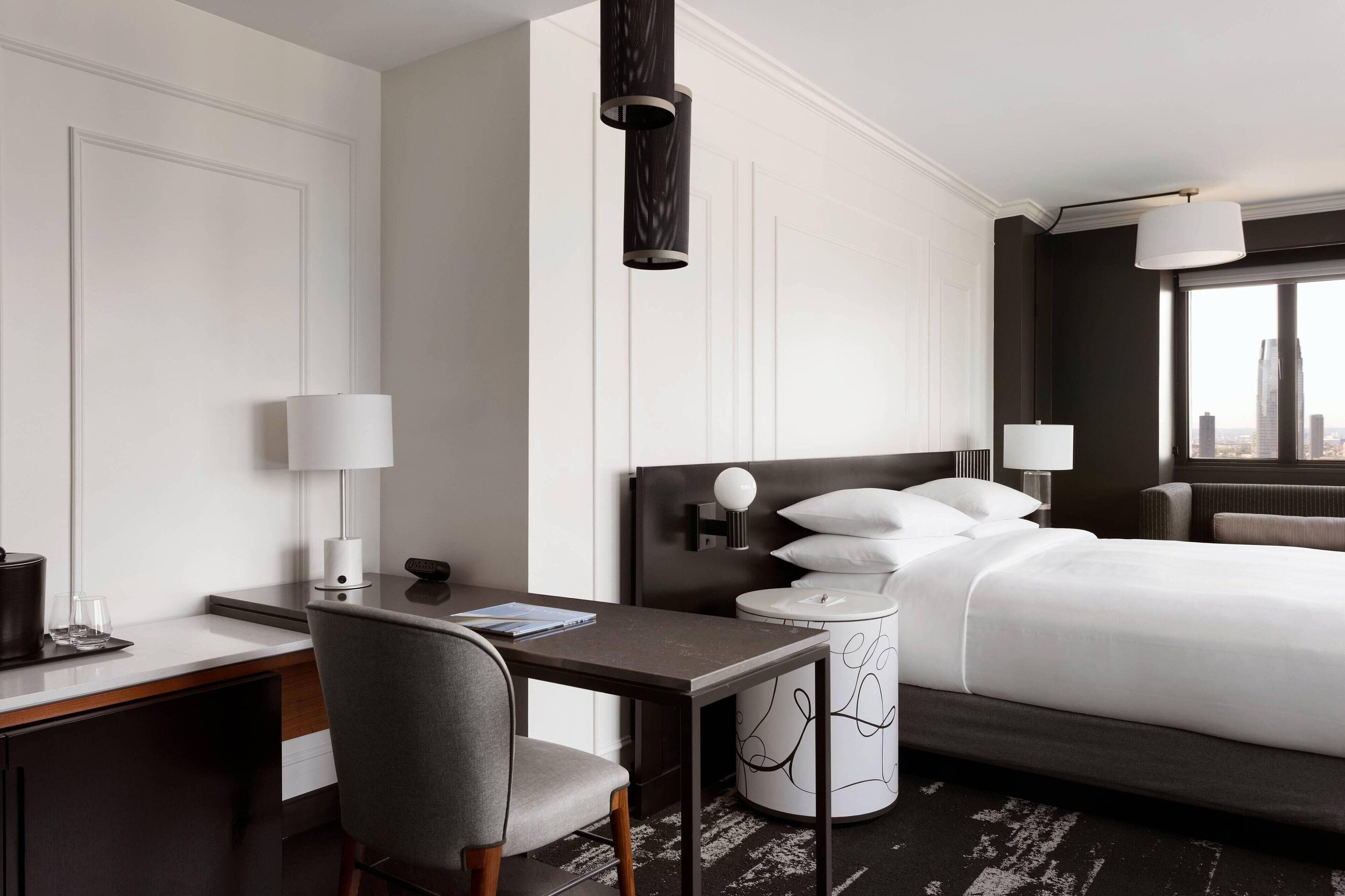Een moderne hotelkamer met een groot bed, een bureau met een stoel, een lamp en uitzicht op de stad.