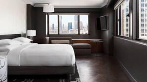 A modern hotel room with a large bed, a seating area, a TV, and a city view. - New York Marriott Downtown (New York)