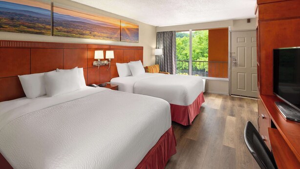 Habitación de hotel con dos camas, televisión, ventana grande con vistas y un cuadro en la pared.