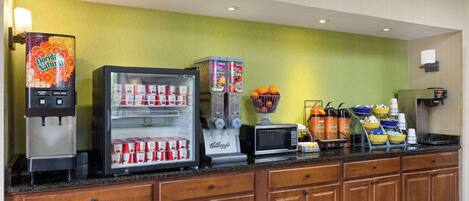 A hotel breakfast area with a vending machine, refrigerator, microwave, and various food items.