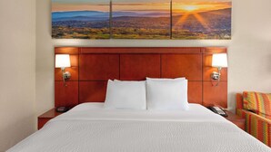 Habitación de hotel con una cama grande, dos lámparas de noche, una mesita de noche con un teléfono y una silla colorida.
