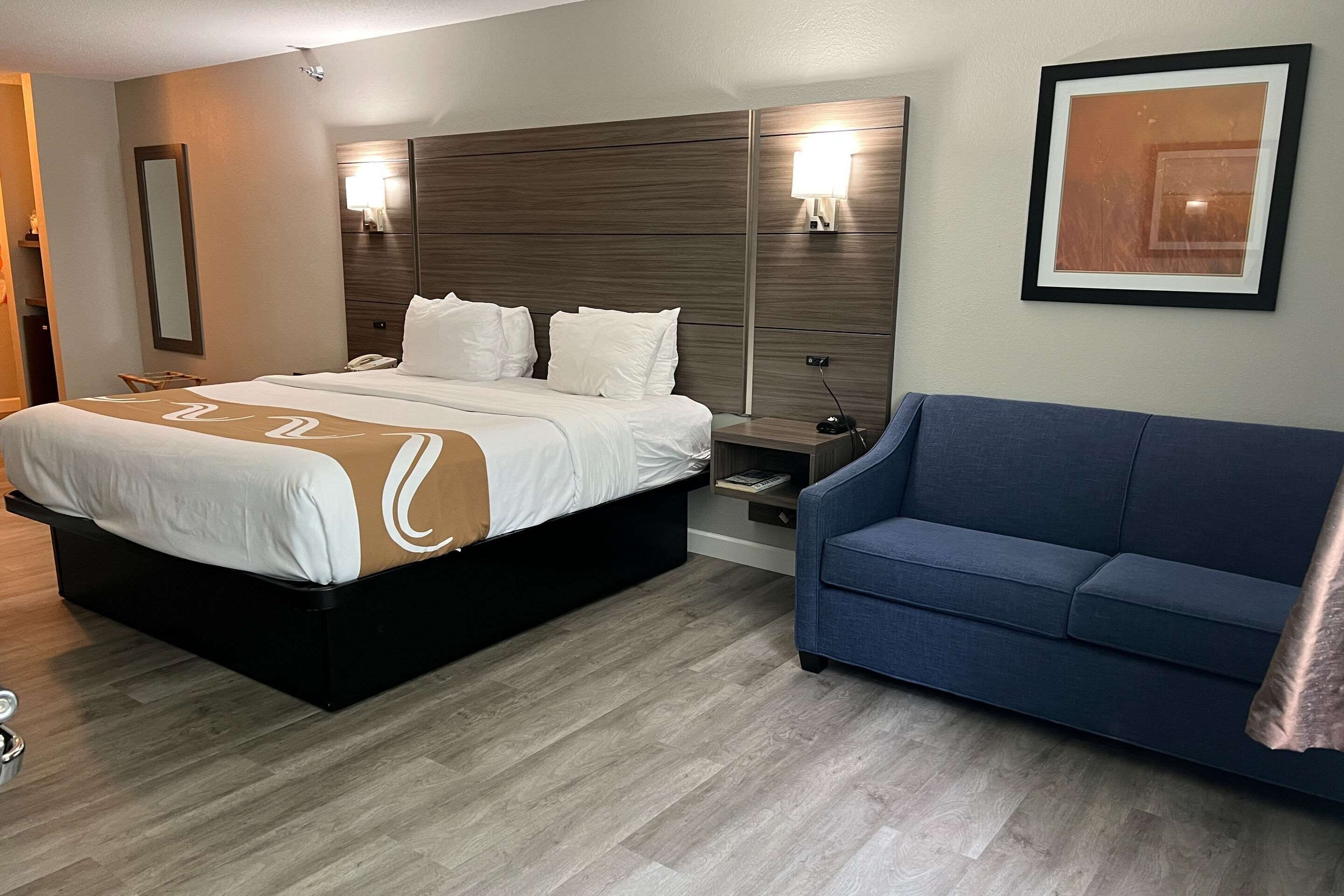 Une chambre d’hôtel avec un grand lit, une table de chevet, une commode, un canapé bleu et un tableau encadré au mur.