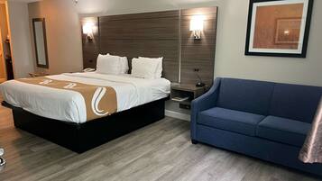 A hotel room with a large bed, a bedside table, a nightstand, a blue sofa, and a framed picture on the wall.
