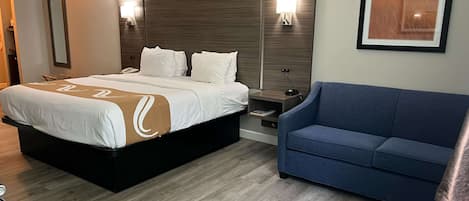 Una habitación de hotel con una cama grande, una mesita de noche, un sofá azul y un cuadro en la pared.