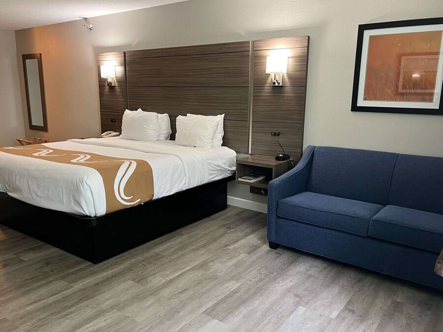 A hotel room with a large bed, a bedside table, a nightstand, a blue sofa, and a framed picture on the wall.