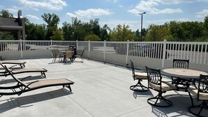 An outdoor patio with lounge chairs and a round table, surrounded by a white fence.