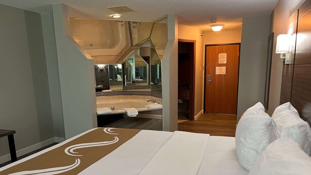 A hotel room with a bed, a bathroom with a sink and mirror, and a door leading to another room.