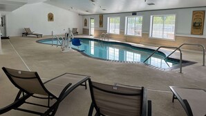 A swimming pool with lounge chairs and a lifeguard chair, surrounded by windows and a wooden wall.