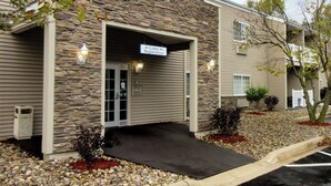 A building with a stone facade, a lobby registration sign, and a parking area with gravel and plants.