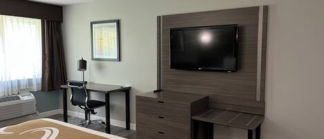 Habitación de hotel con cama, escritorio, silla, televisor y ventana con cortinas.