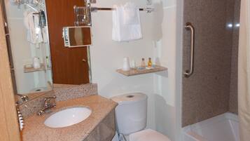 A bathroom with a granite countertop sink, a toilet, a shower with a grab bar, and a towel rack with folded towels.