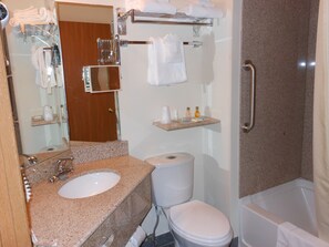 A bathroom with a granite countertop sink, a toilet, a shower with a grab bar, and a towel rack with folded towels.