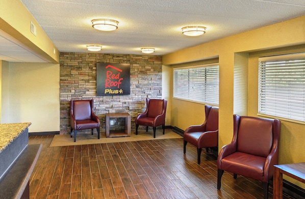 A reception area with a stone wall, a Red Roof Plus sign, and four leather chairs.