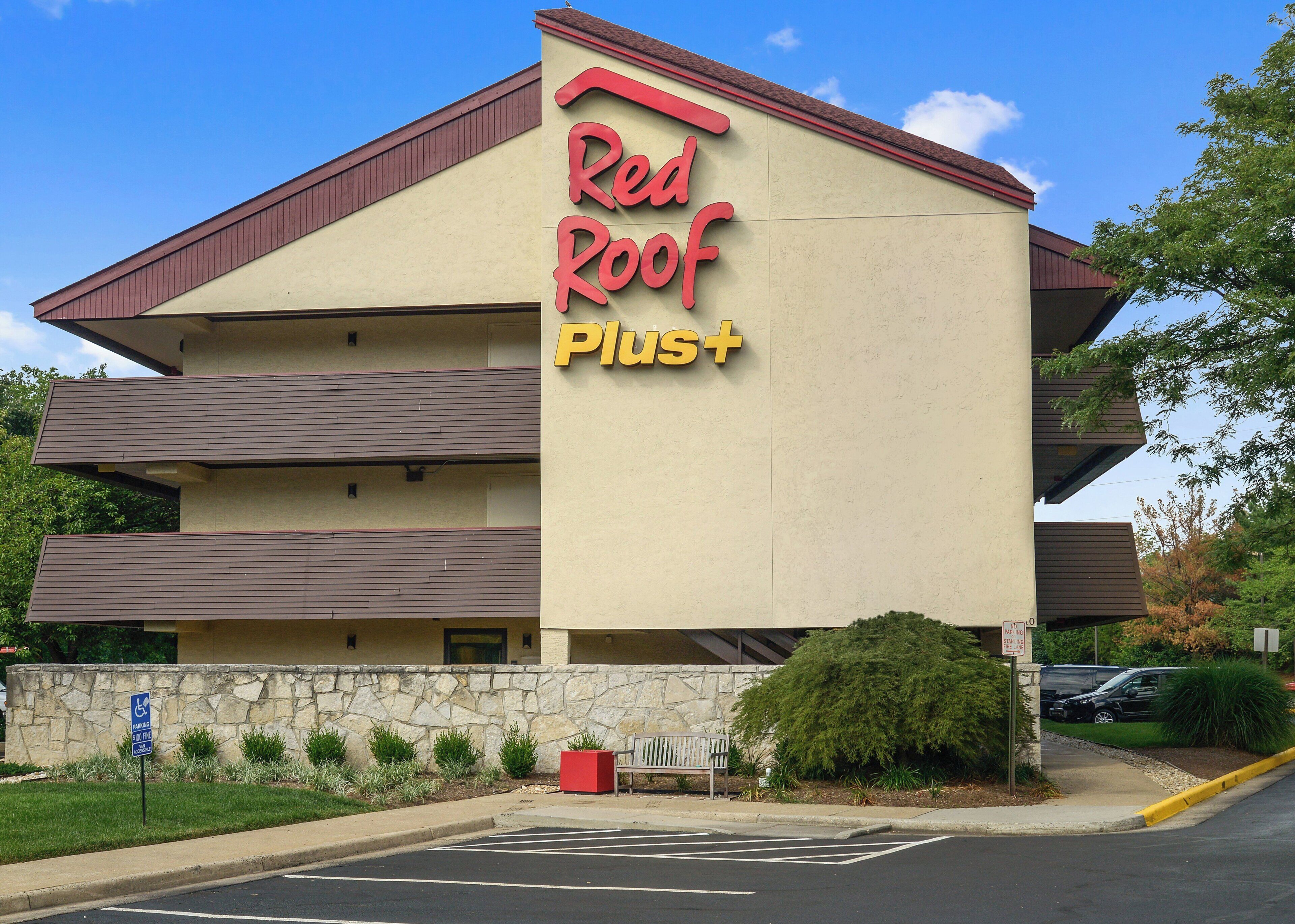A Red Roof Plus hotel with a stone facade, multiple balconies, and a parking lot.