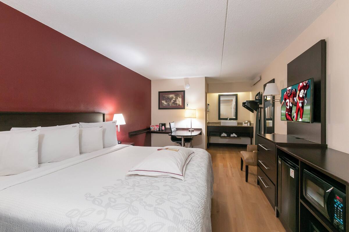 A hotel room with a large bed, a desk, a chair, a television, a microwave, and a small kitchenette.