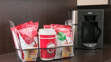 A coffee maker and a basket with coffee pods and a disposable cup on a wooden surface.