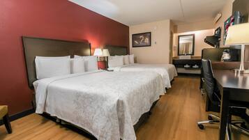 A hotel room with two beds, a desk, a chair, a lamp, and a mirror.