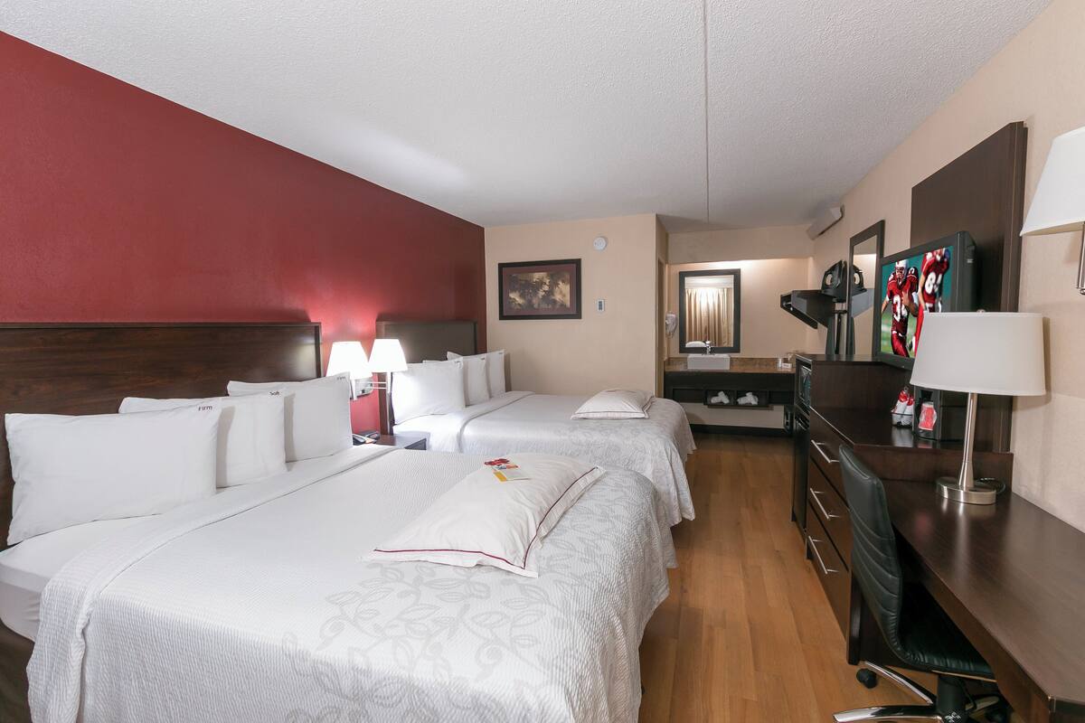 A hotel room with two beds, a desk, a chair, and a dresser.