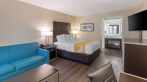 Une chambre d’hôtel avec un lit, un canapé bleu, un bureau, une télévision et une salle de bain visible à travers une porte ouverte.