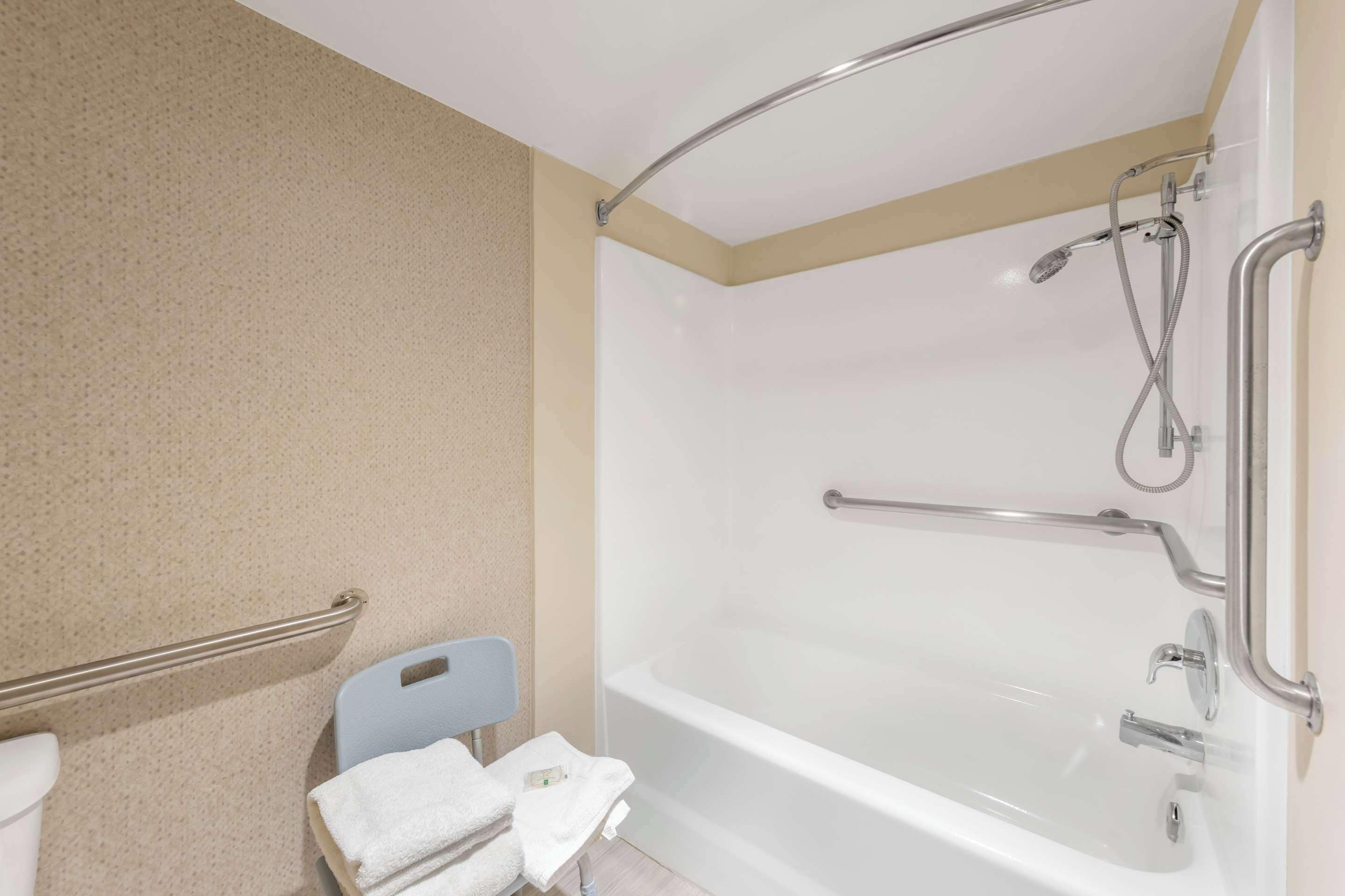 A bathroom with a bathtub, a shower, and a handrail.