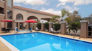 Une piscine entourée de chaises longues et de parasols, le tout bordé par un bâtiment doté d’arches et d’un toit en tuiles.