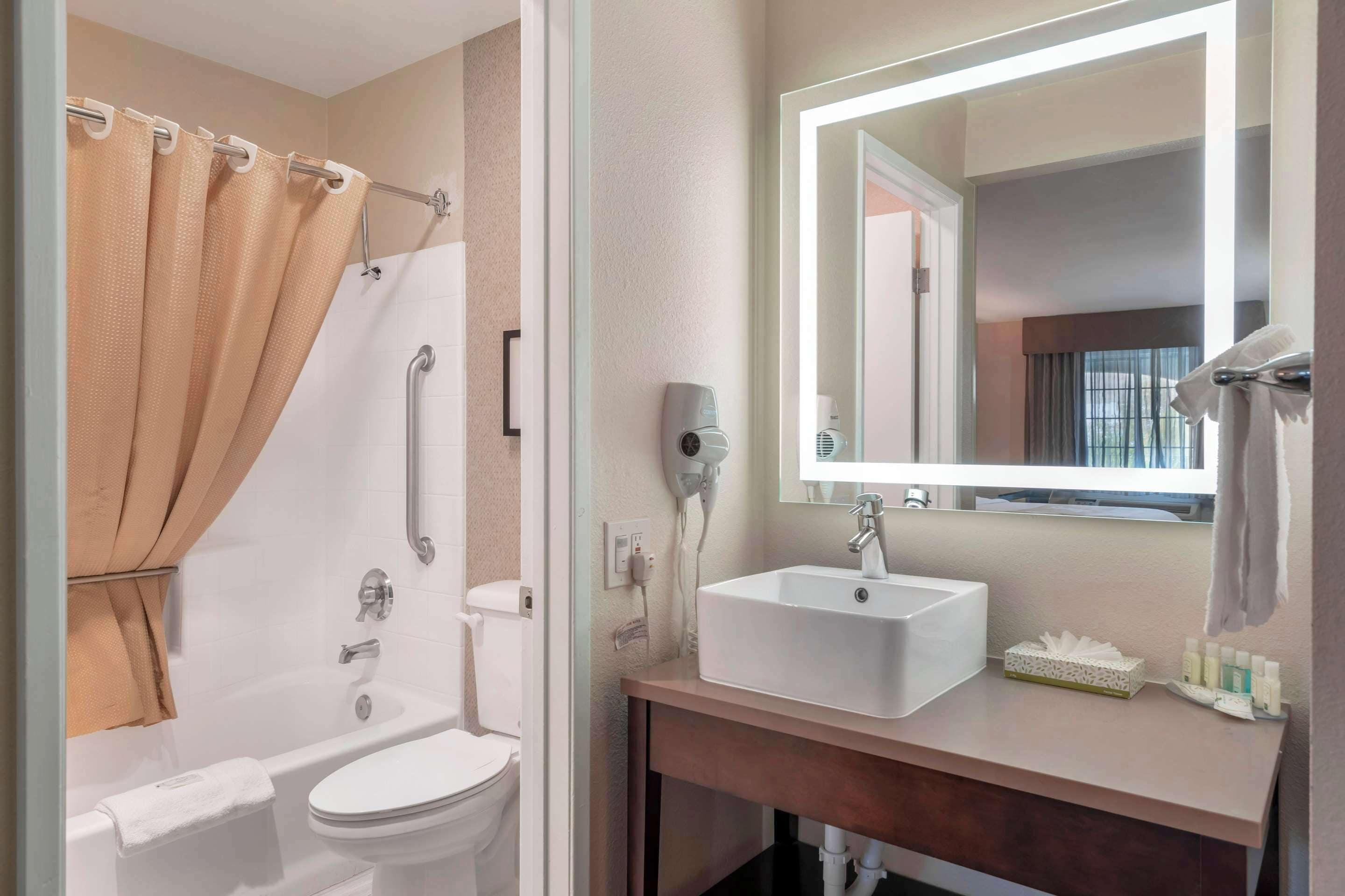 A bathroom with a bathtub, toilet, and sink, equipped with a hairdryer and a mirror.