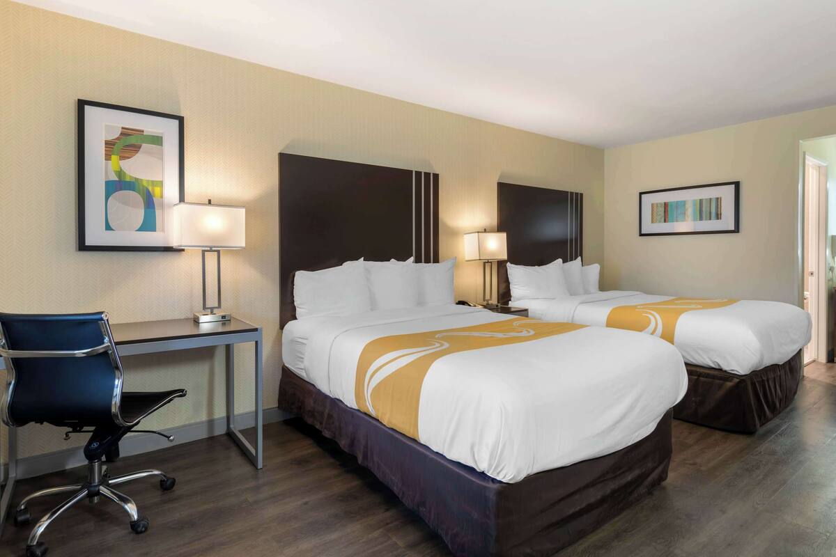 Quarto de hotel com duas camas, uma mesa e uma cadeira.