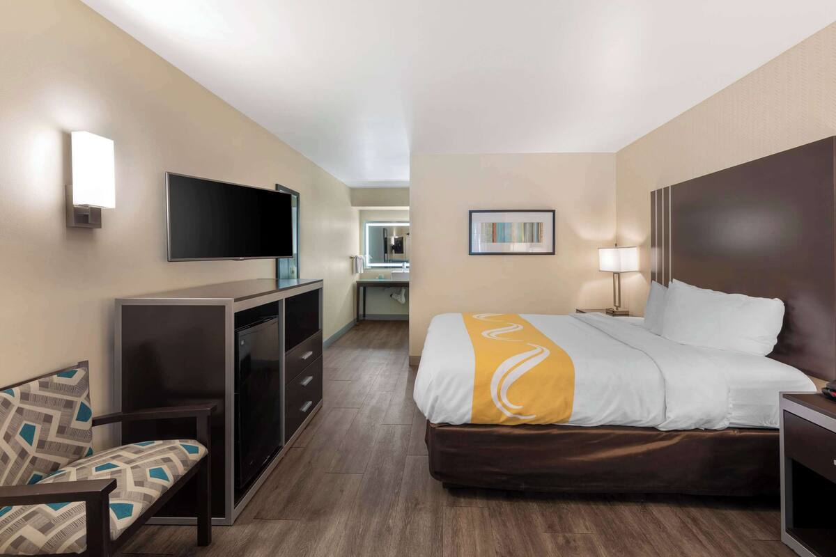 Quarto de hotel com cama, televisão, escrivaninha e cadeira.